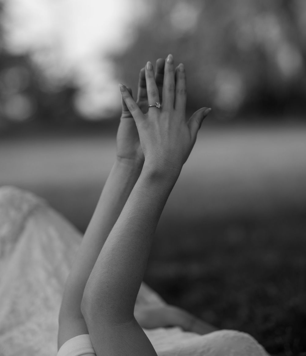 Black and white photo of two raised arms with an engagement ring visible on one hand outdoors.
