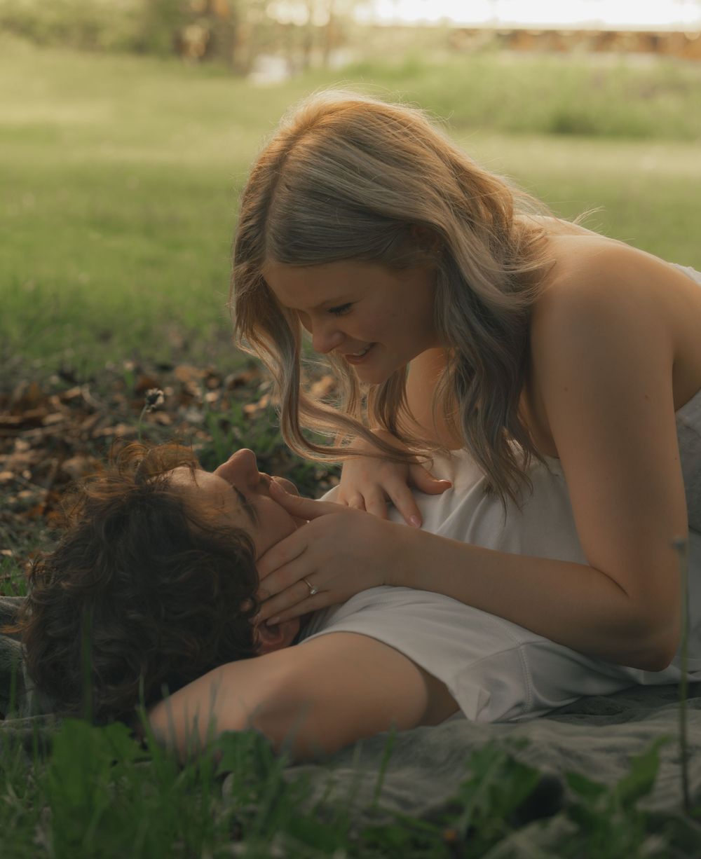 Couple sharing an intimate romantic moment together lying in green grass during golden hour.