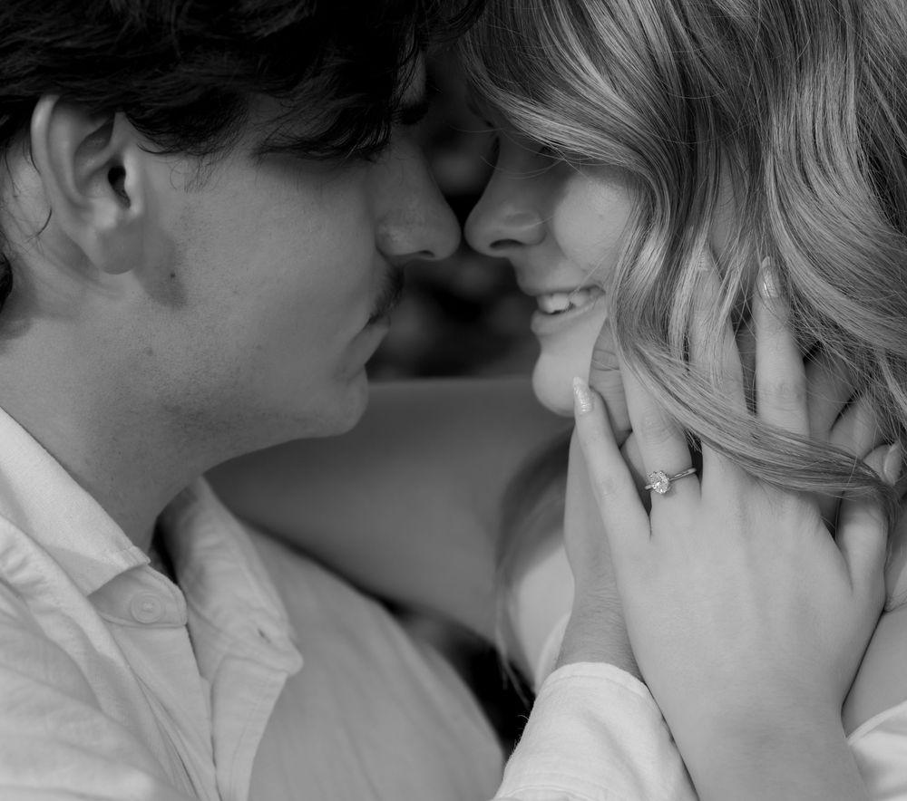 Black and white photo of a romantic couple sharing an intimate moment, nearly kissing, woman wearing a ring.