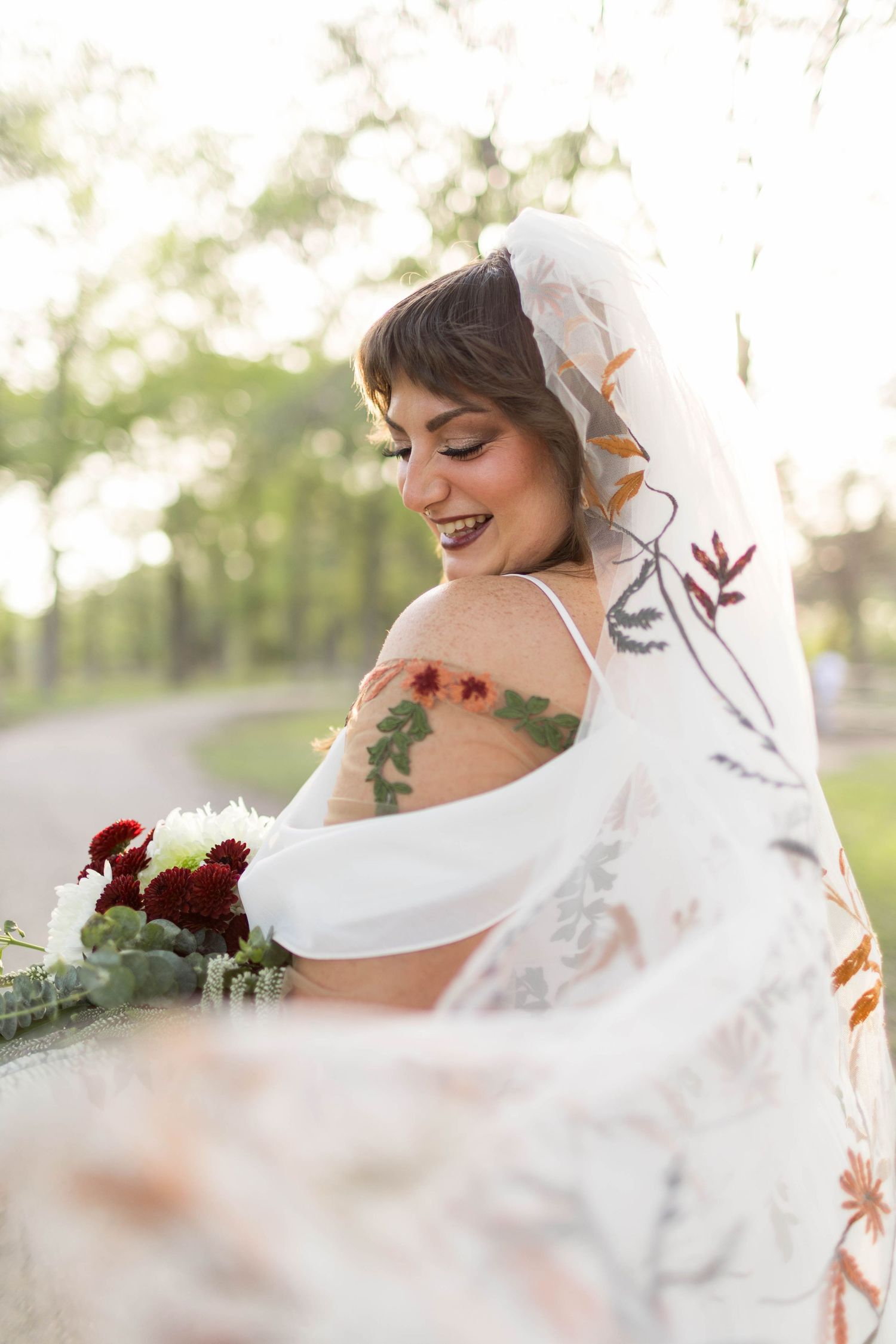 Bride in white wedding dress and veil twirling on a sunlit forest path, arms outstretched, motion blur capturing joyful movement.