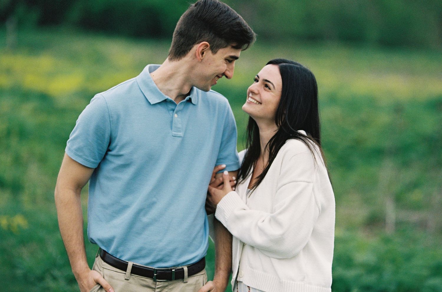 Happy couple smiling at each other in a green field, man in blue polo and woman in white jacket.