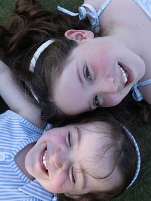Two smiling children lying on grass, a girl with a white headband and a younger boy in a blue striped shirt.