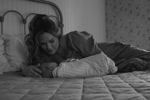 Black and white photo of a woman lying on a bed tenderly cradling a newborn baby.
