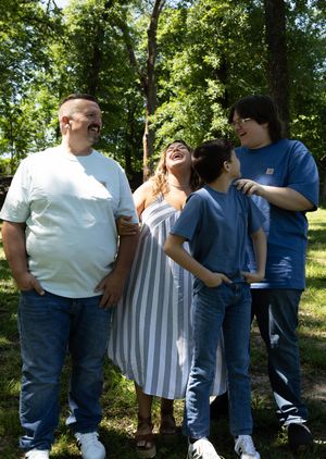 Family of four laughing together outdoors in a lush green park on a sunny day.