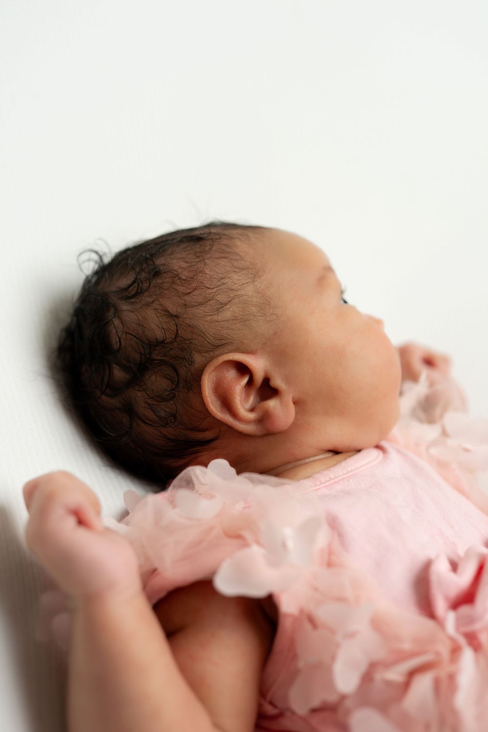 Close-up profile of newborn baby in pink floral dress on white background.