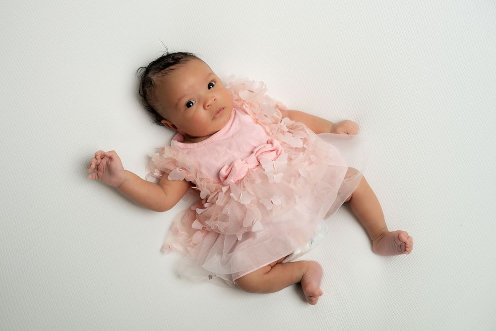 Newborn baby girl in a pink ruffled dress lying on a clean white background.