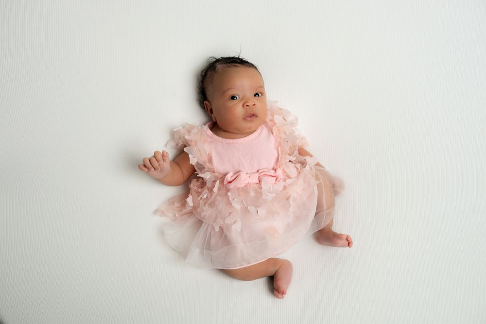 Adorable infant in a pink ruffle dress posed on a white studio backdrop.
