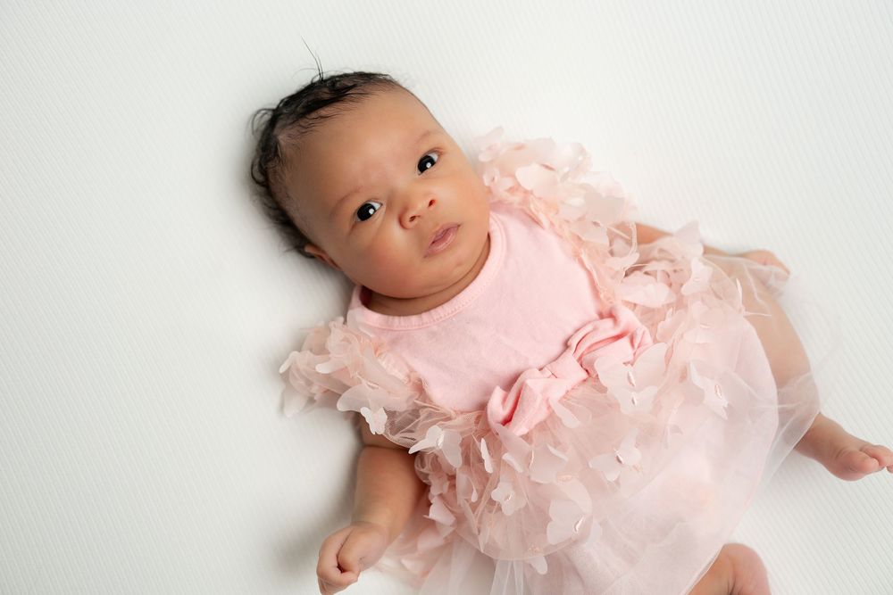 Adorable newborn baby in a pink ruffled tutu dress lying on a white backdrop.