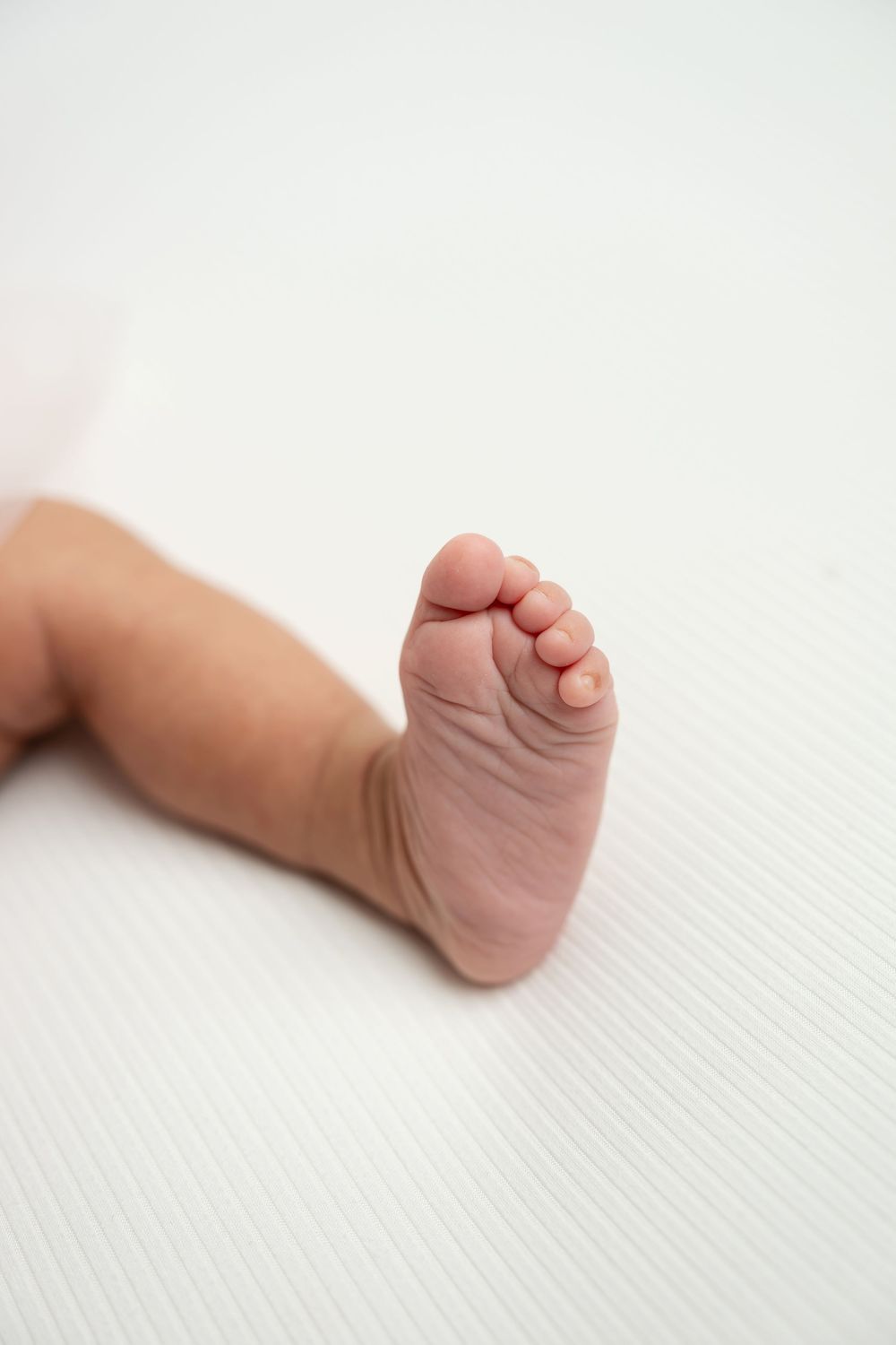 Close-up of a newborn baby's tiny foot and toes resting on a white surface.