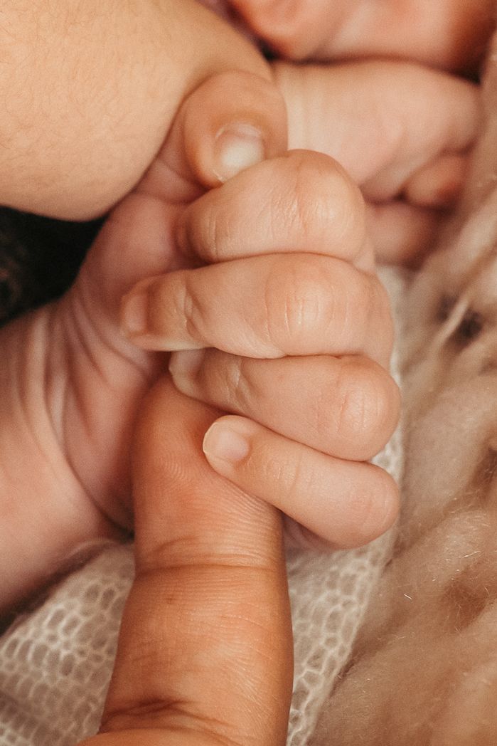 Mano de un recién nacido sujetando el dedo de su madre durante una sesión de fotografía natural de newborn en Girona.