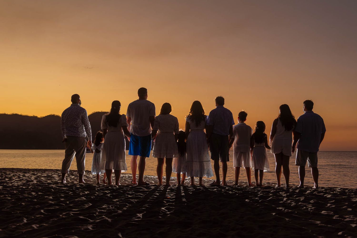 Silhouette of a large family holding hands on a beach at sunset with golden sky.