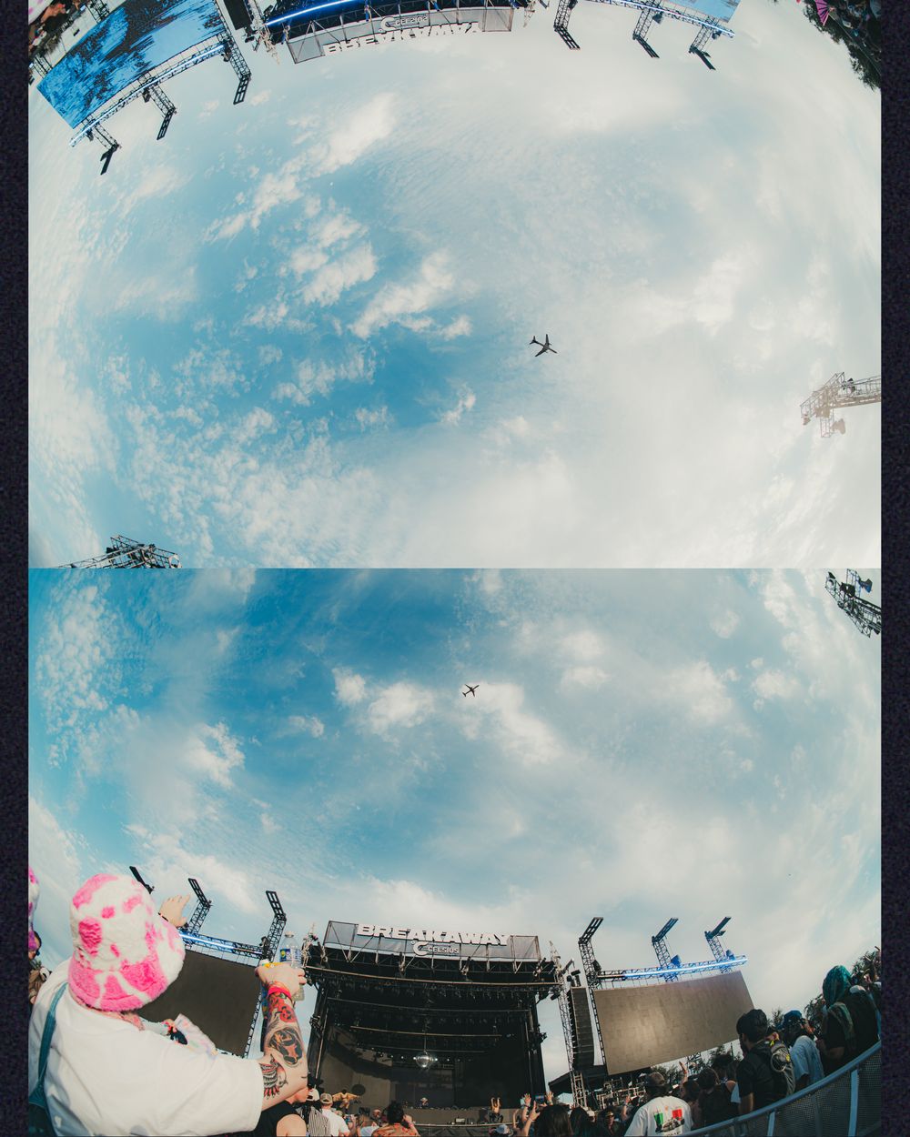 Fisheye lens view of an outdoor music festival stage with crowds, large screens, and a plane flying overhead in a blue sky.