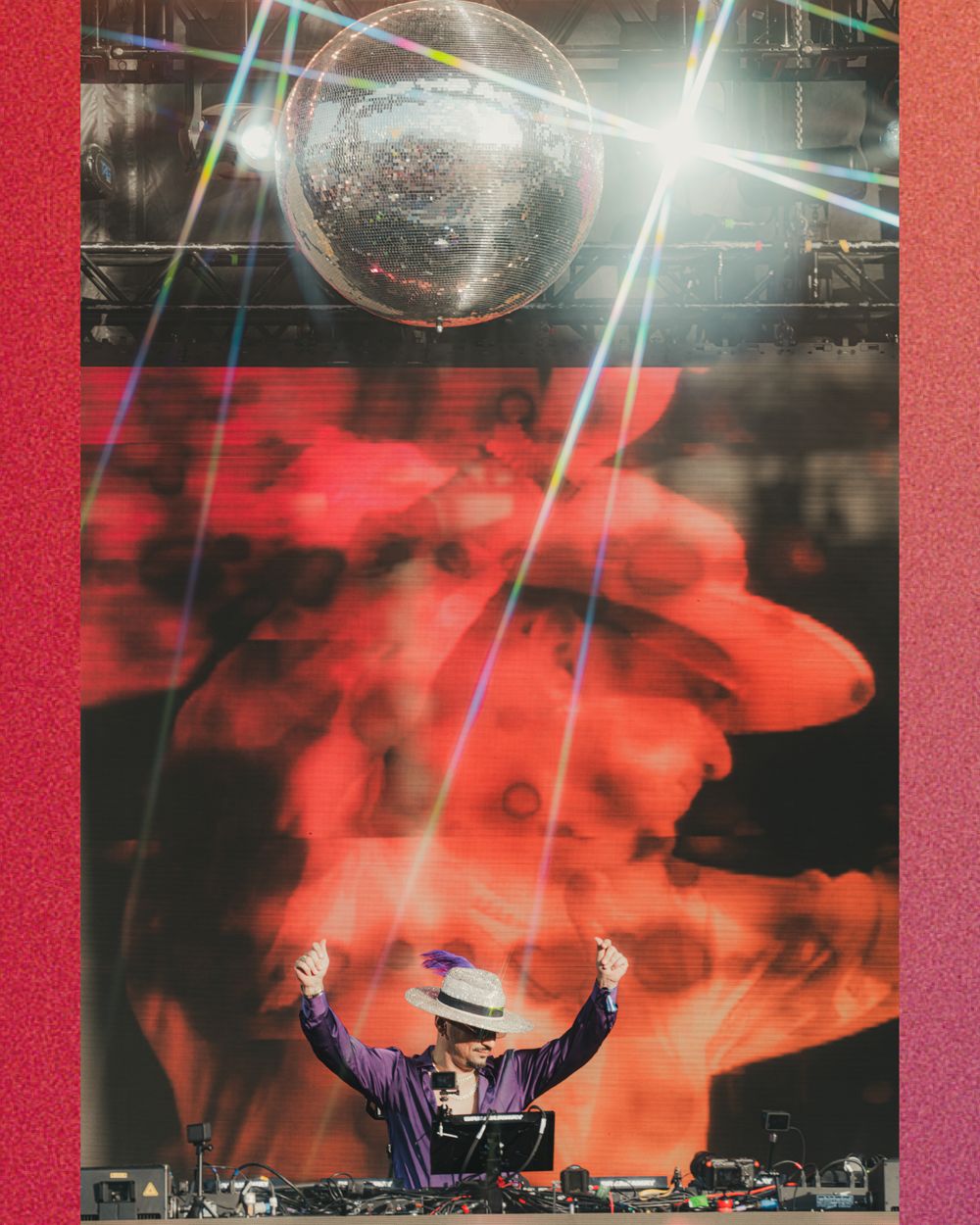 DJ performing on stage under a disco ball with colorful laser lights and a vibrant red smoke visual backdrop.