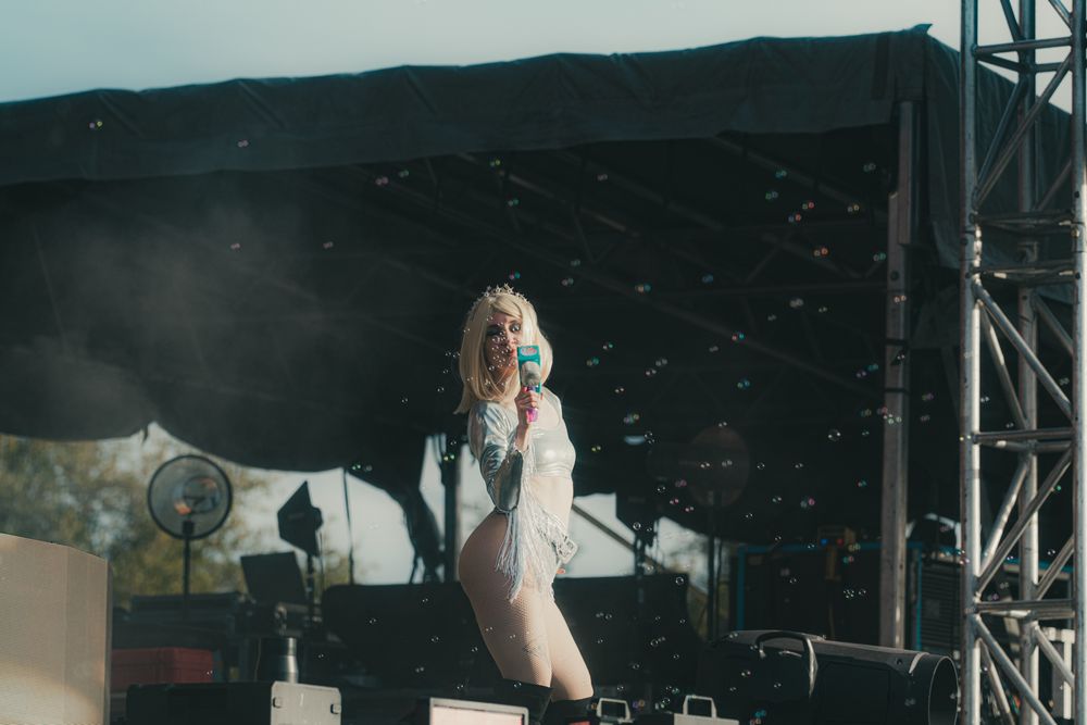 Blonde female performer singing on outdoor festival stage wearing white outfit with confetti falling around her.