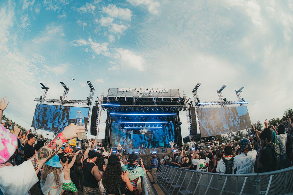 Crowd enjoying an outdoor music festival with a large illuminated stage under a dramatic blue sky.