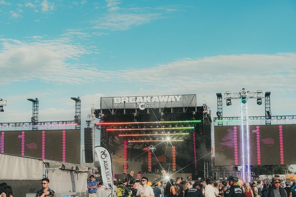 Breakaway Music Festival outdoor stage with colorful lights and crowd under a blue sky.