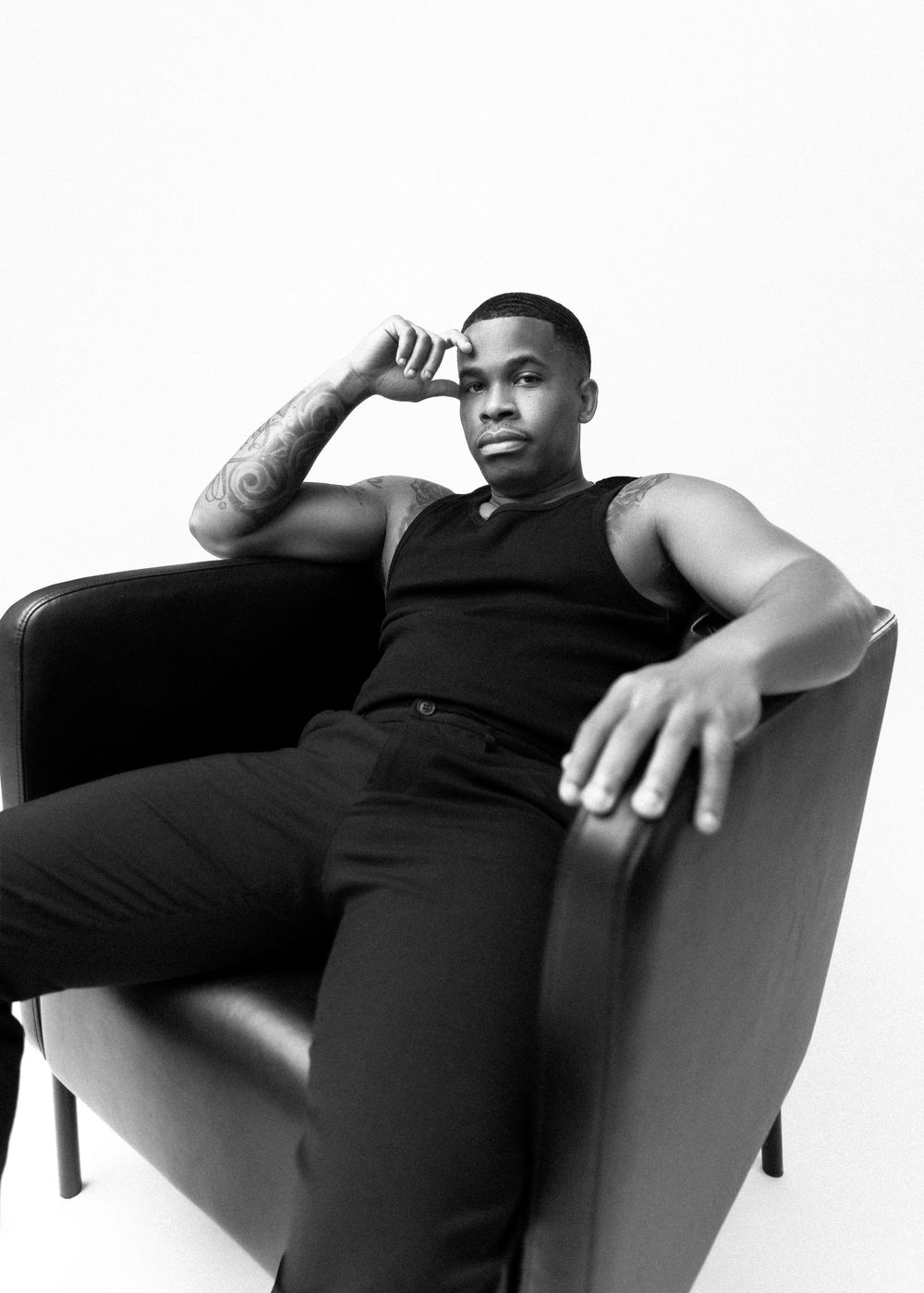 Black and white portrait of a muscular person in a black tank top lounging in an armchair.