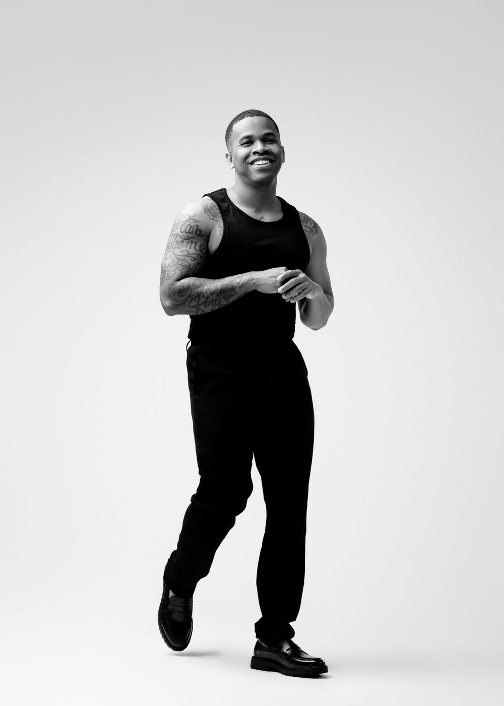 Black and white portrait of someone posing in athletic wear with a joyful expression against a plain background.
