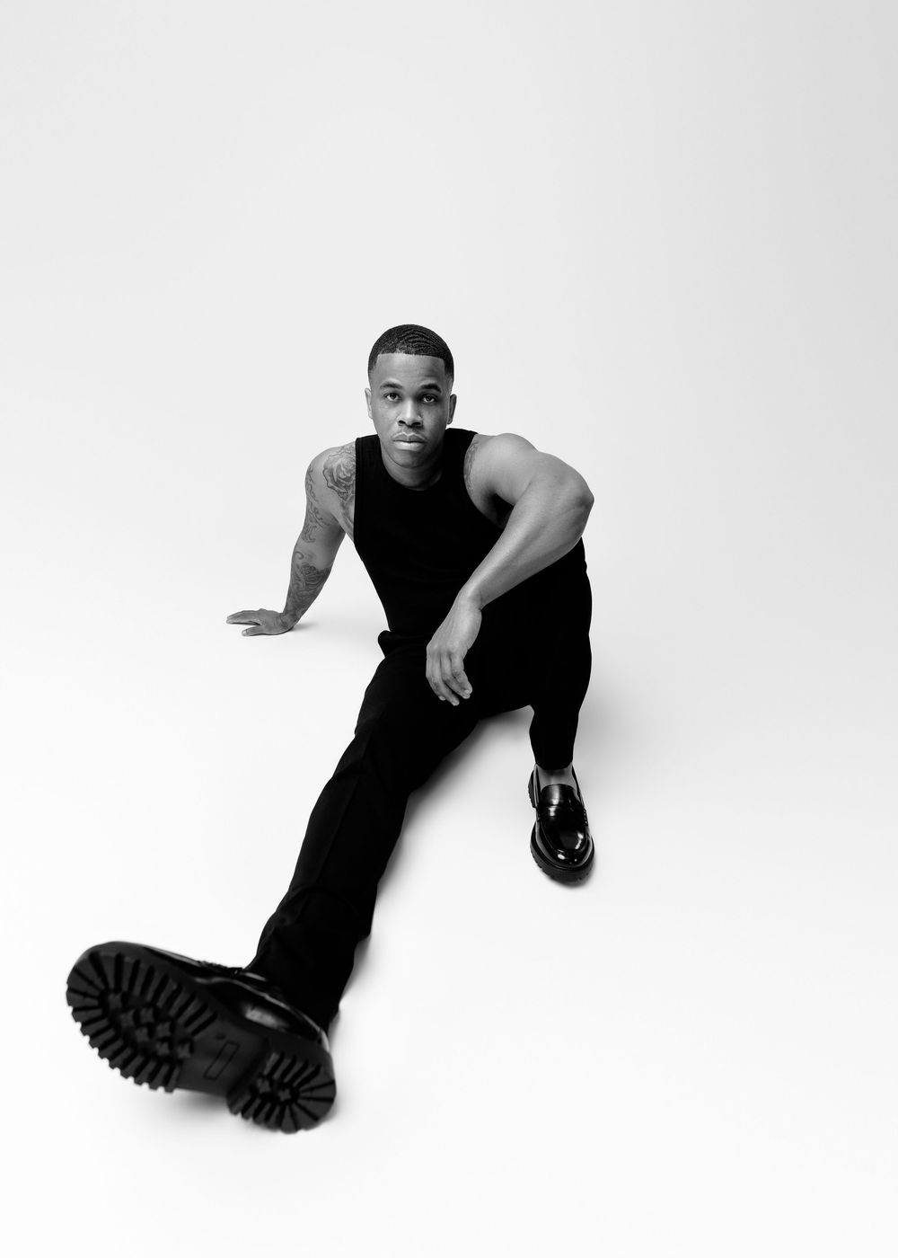 Black and white fashion photo of a person in dark clothing posing on the ground wearing chunky boots.