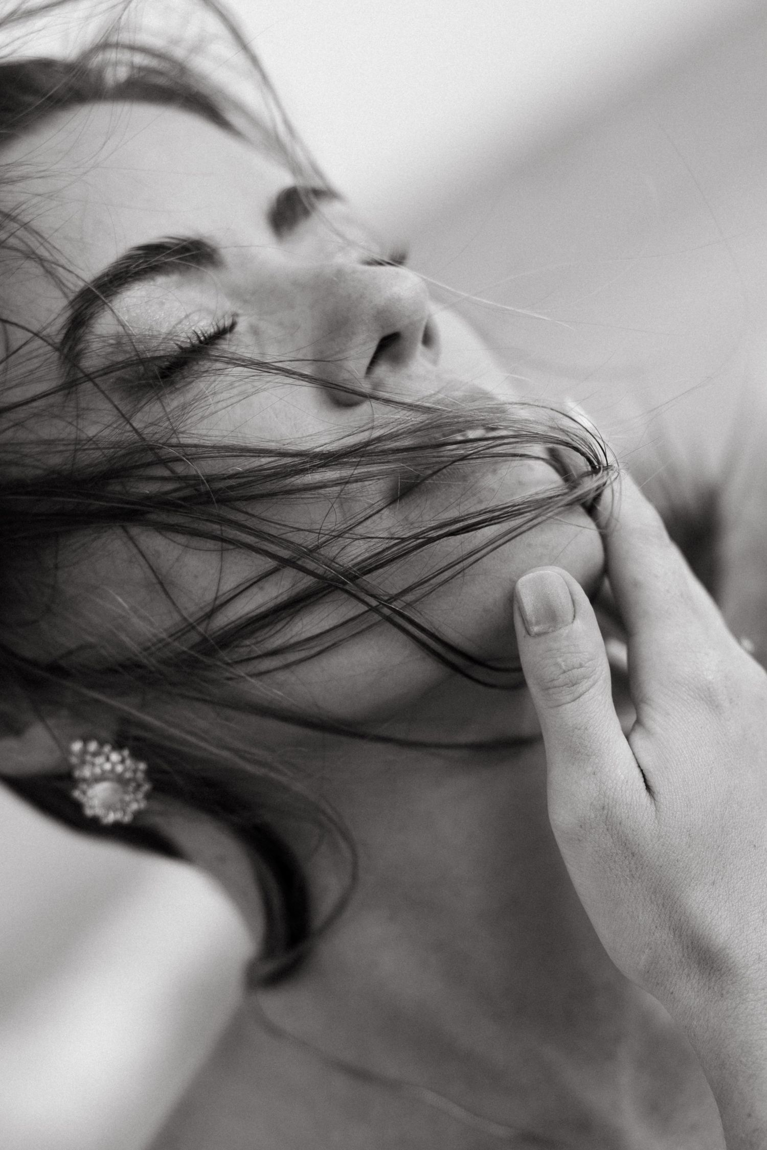 Artistic black and white close-up of a woman with wind-blown hair across her face and pearl earring.