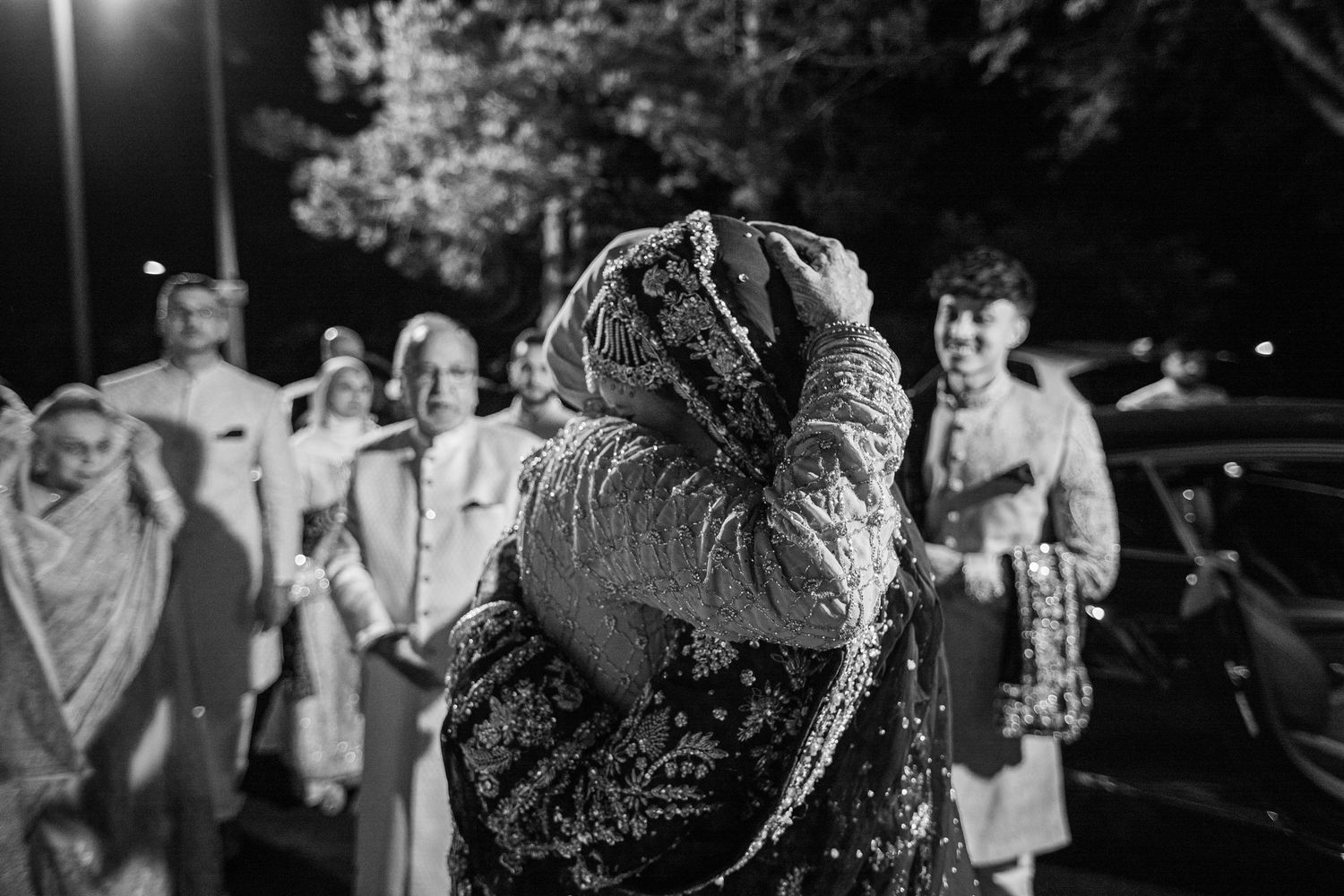 Indian wedding ceremony with bride in pink lehenga and groom in cream sherwani exchanging garlands surrounded by family.