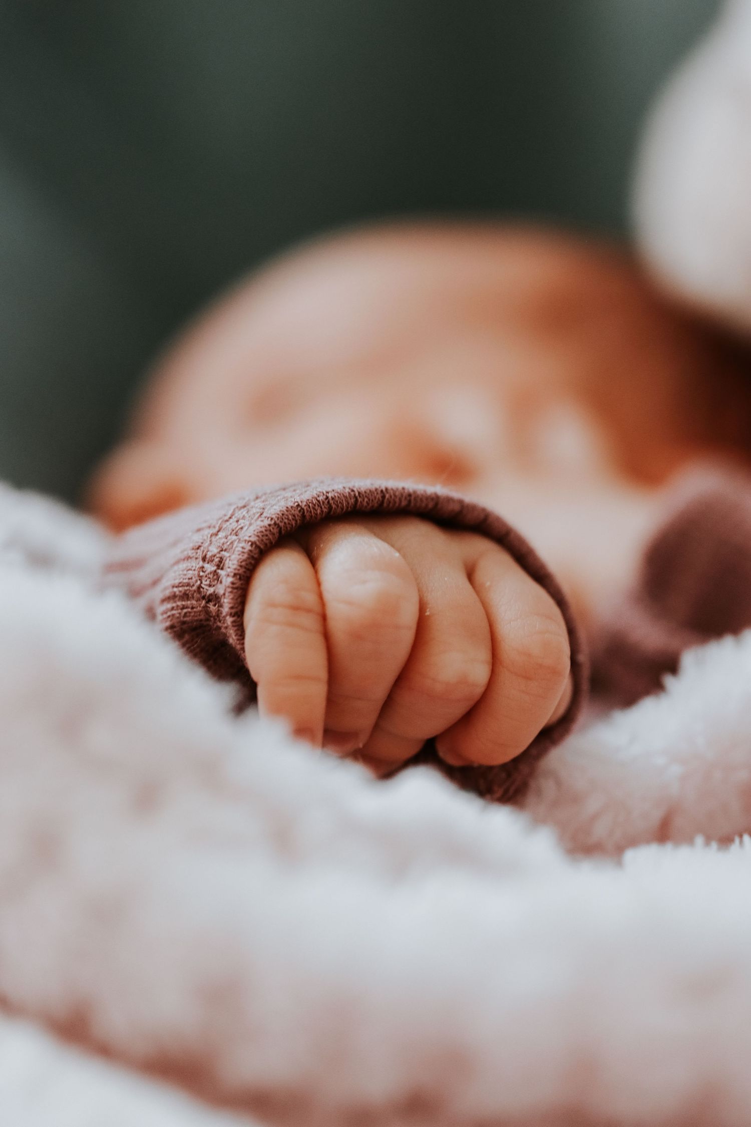 Close-up of a sleeping newborn baby's tiny hand resting on a soft white blanket.