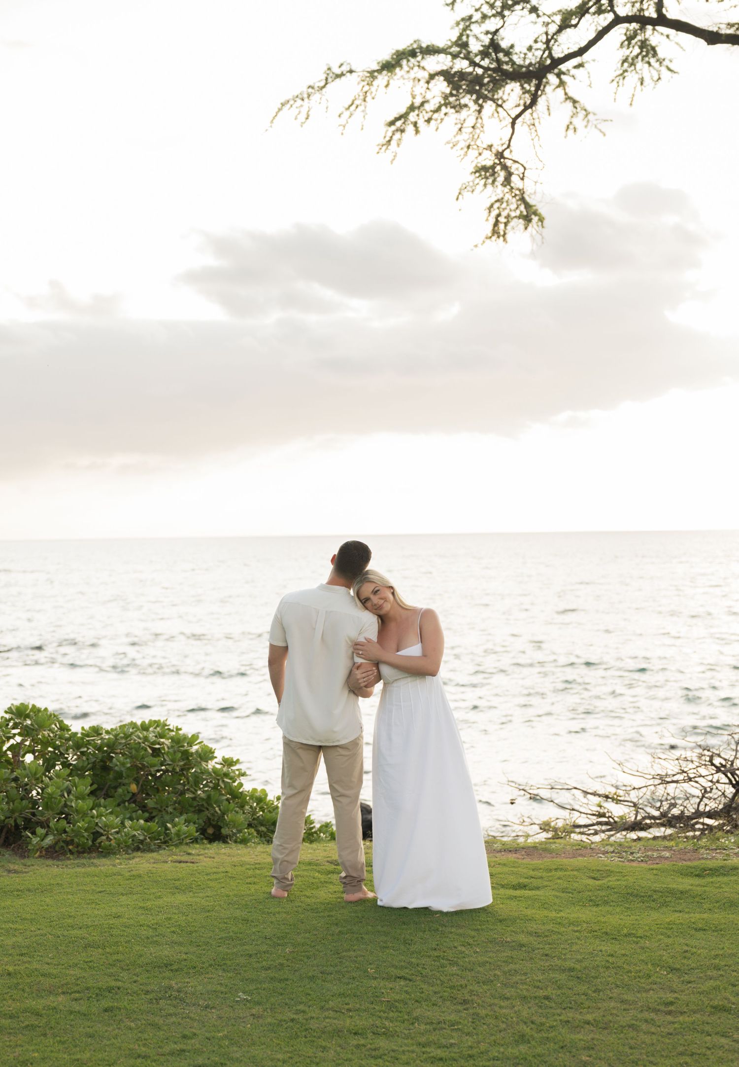 Couple holding hands walking barefoot on a sandy tropical beach, woman in white dress, man in white shirt and khaki pants.