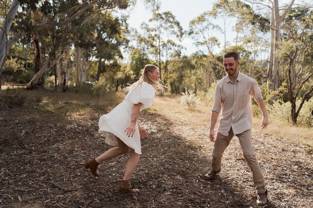 A joyful couple dancing playfully in a sunlit Australian bush setting surrounded by eucalyptus trees in rouse hill photoshoot