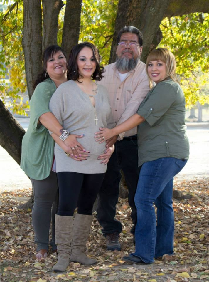 A family of four, placing hands on an expectant mother's pregnant belly.