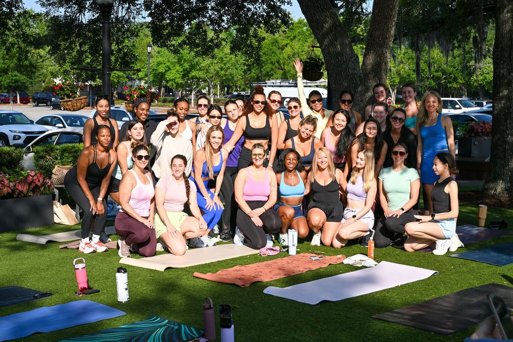 Large group of women posing together on yoga mats outdoors on green grass during a sunny day yoga class event.