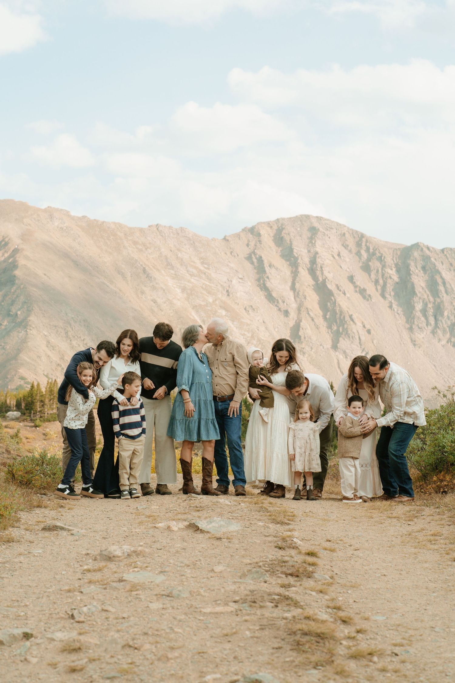 Large multigenerational family portrait outdoors with mountain backdrop on a sunny day.