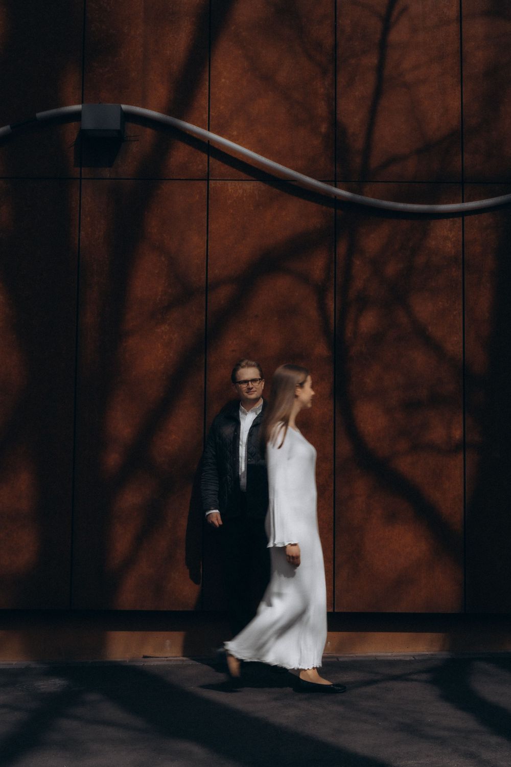 Editorial engagement portrait of a couple standing together in warm evening light among tree shadows by the wall in Helsinki