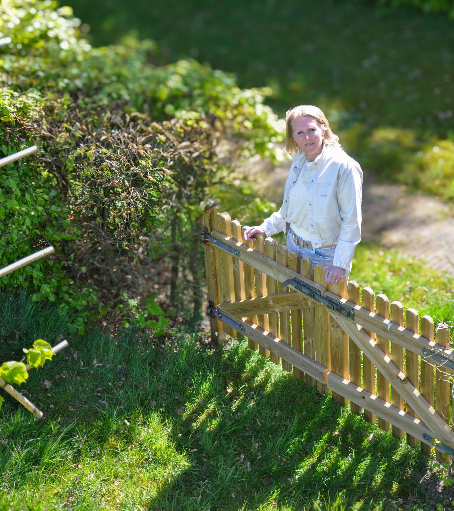 Woman in blue shirt leaning on wooden picket fence in lush green garden.