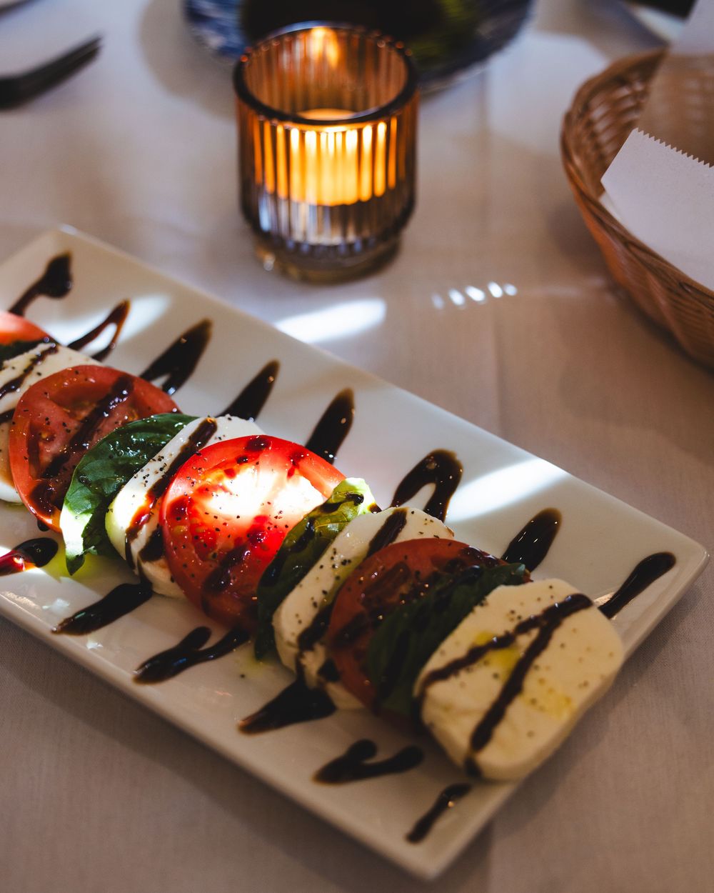 Caprese salad with fresh tomatoes, mozzarella, basil, and balsamic glaze on a white rectangular plate.