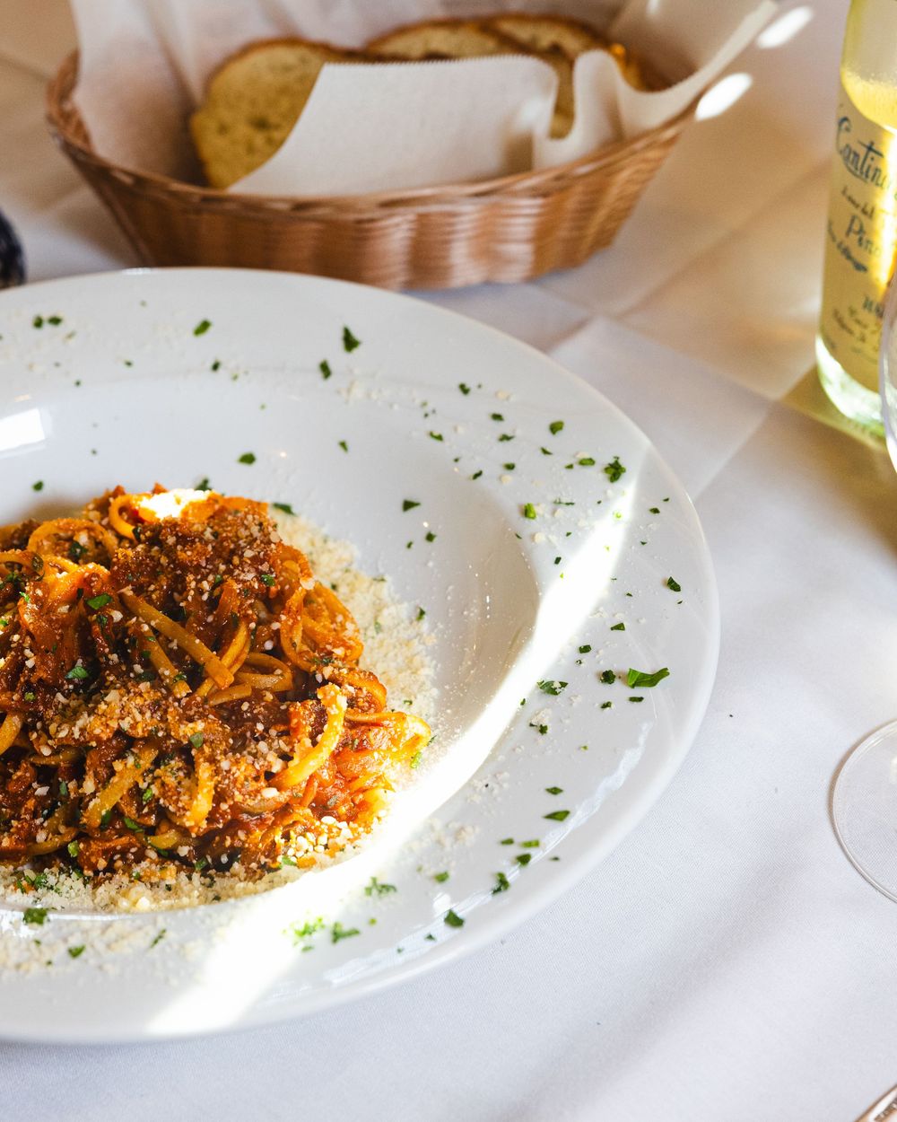 Tagliatelle pasta in tomato meat sauce topped with parmesan and herbs served with bread and white wine.
