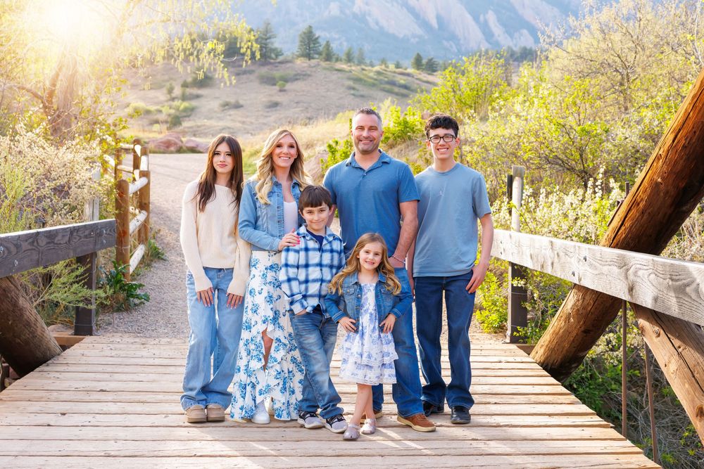Family of six posing on a wooden bridge with mountain backdrop during golden hour in Colorado.