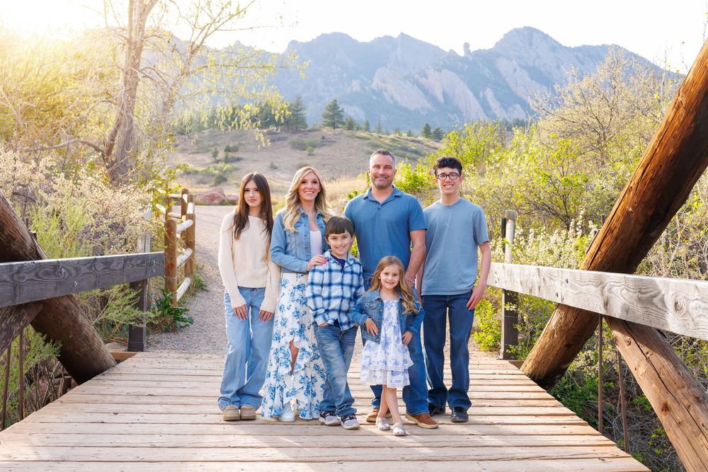 Family of six posing on a wooden bridge with Colorado Flatirons mountains in the background.