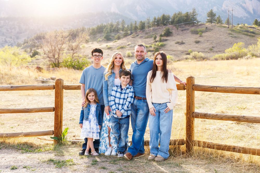 Happy family of six smiling together by a rustic fence with scenic mountain views in Colorado.