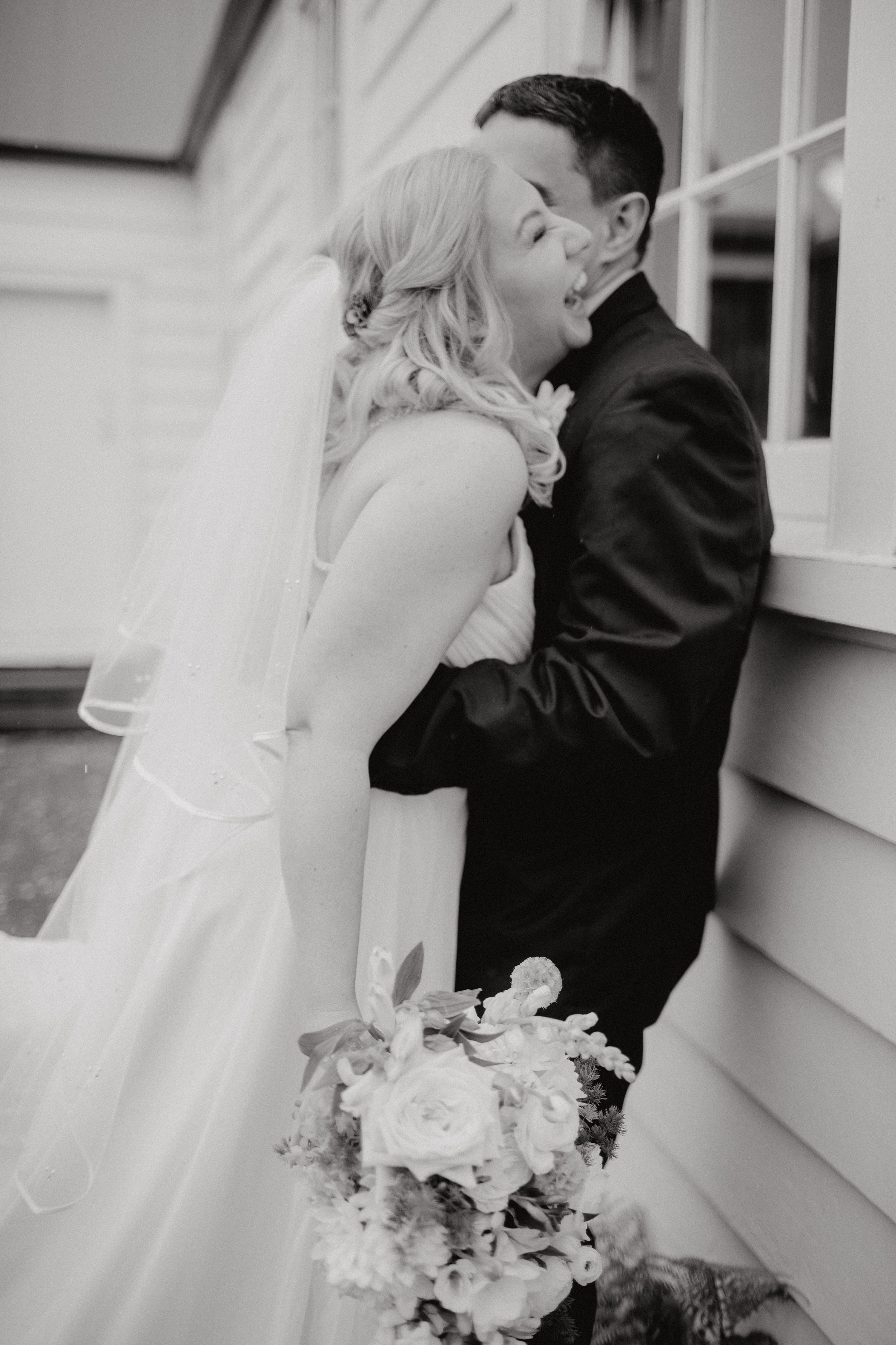 Black and white photo of romantic moment between newlyweds with bridal bouquet.