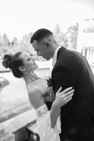 A romantic black and white wedding portrait of a couple in close embrace with the bride wearing a lace dress.