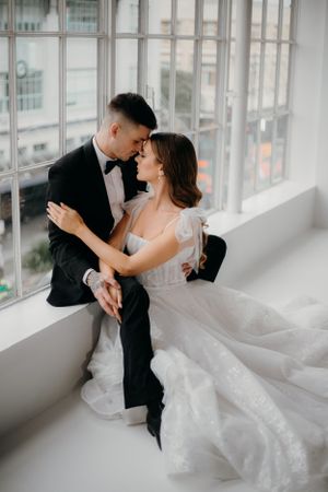 Romantic wedding couple sitting in window ledge sharing intimate moment.