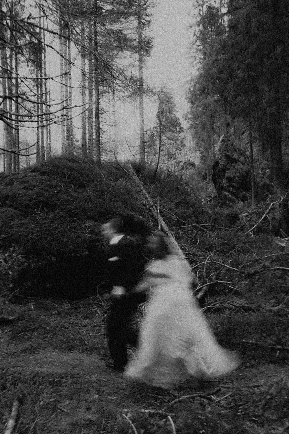 Blurred black and white photo of a bride and groom dancing in a misty forest, creating a dreamy, motion-filled effect.
