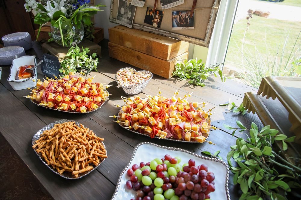 Elegant party food spread with fruit skewers, pretzel sticks, grapes, and fresh greens on a rustic wooden table.