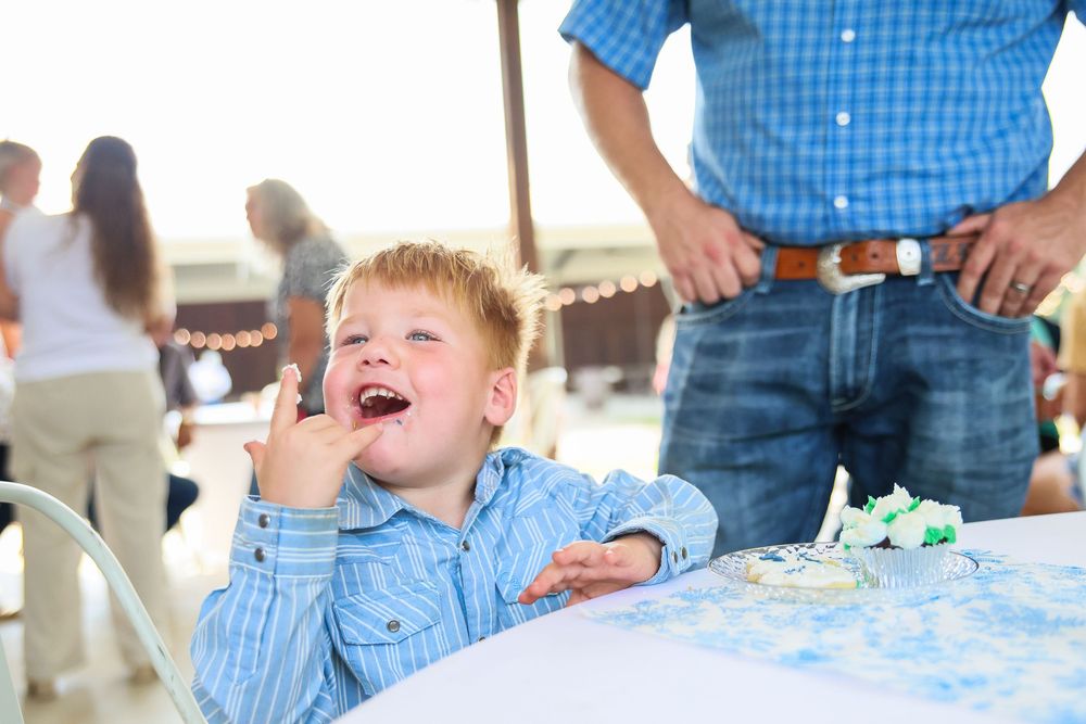 Happy young boy in blue shirt eating cake at a birthday party celebration outdoors.