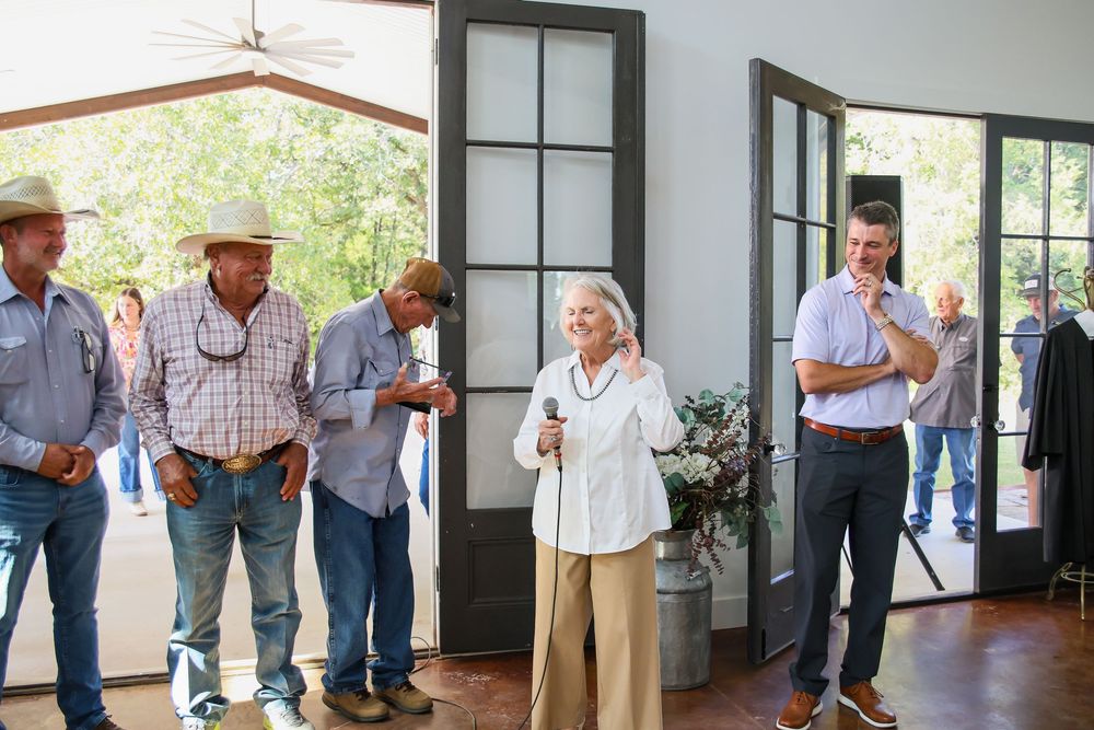 Group of people gathered indoors near open French doors at a casual outdoor ranch event.
