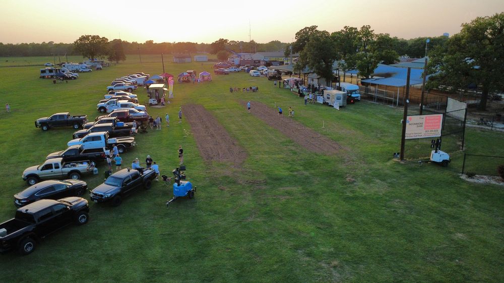 Aerial view of a outdoor community event at sunset with cars lined up on green grass field.