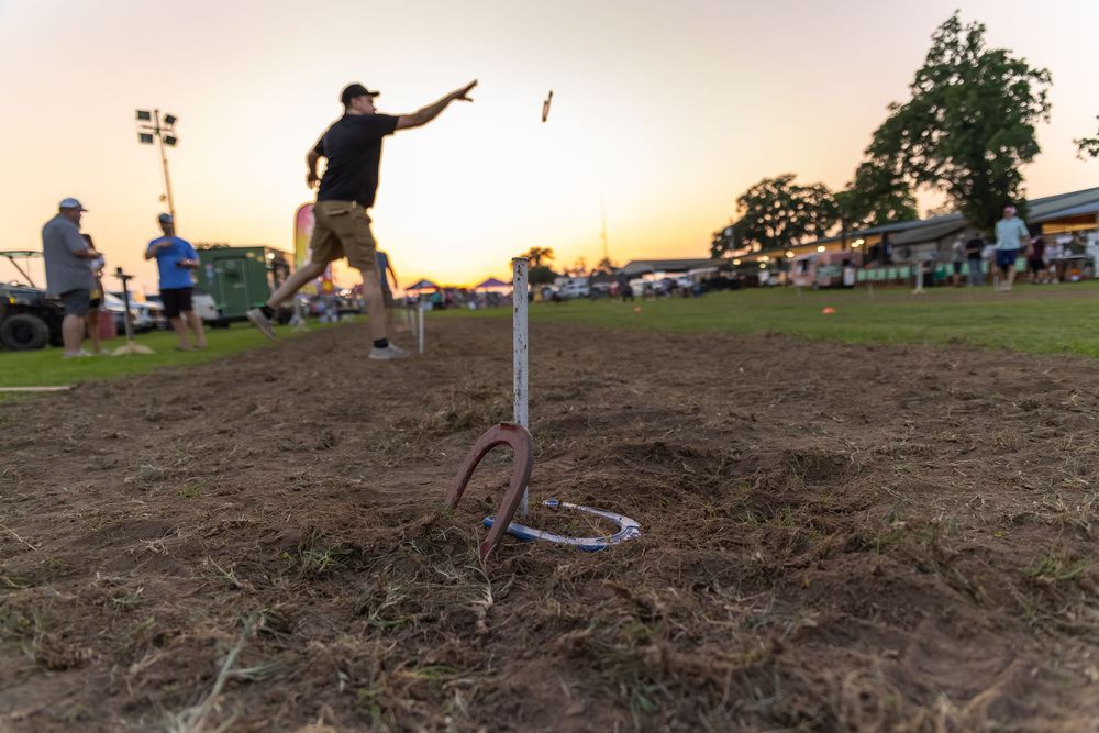 Man throwing horseshoes at sunset on a dirt field during an outdoor horseshoe tournament.