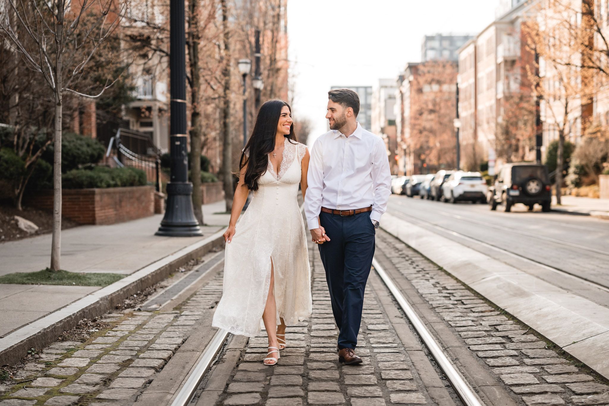 Couple holding hands walking on cobblestone street with tram tracks in urban setting.