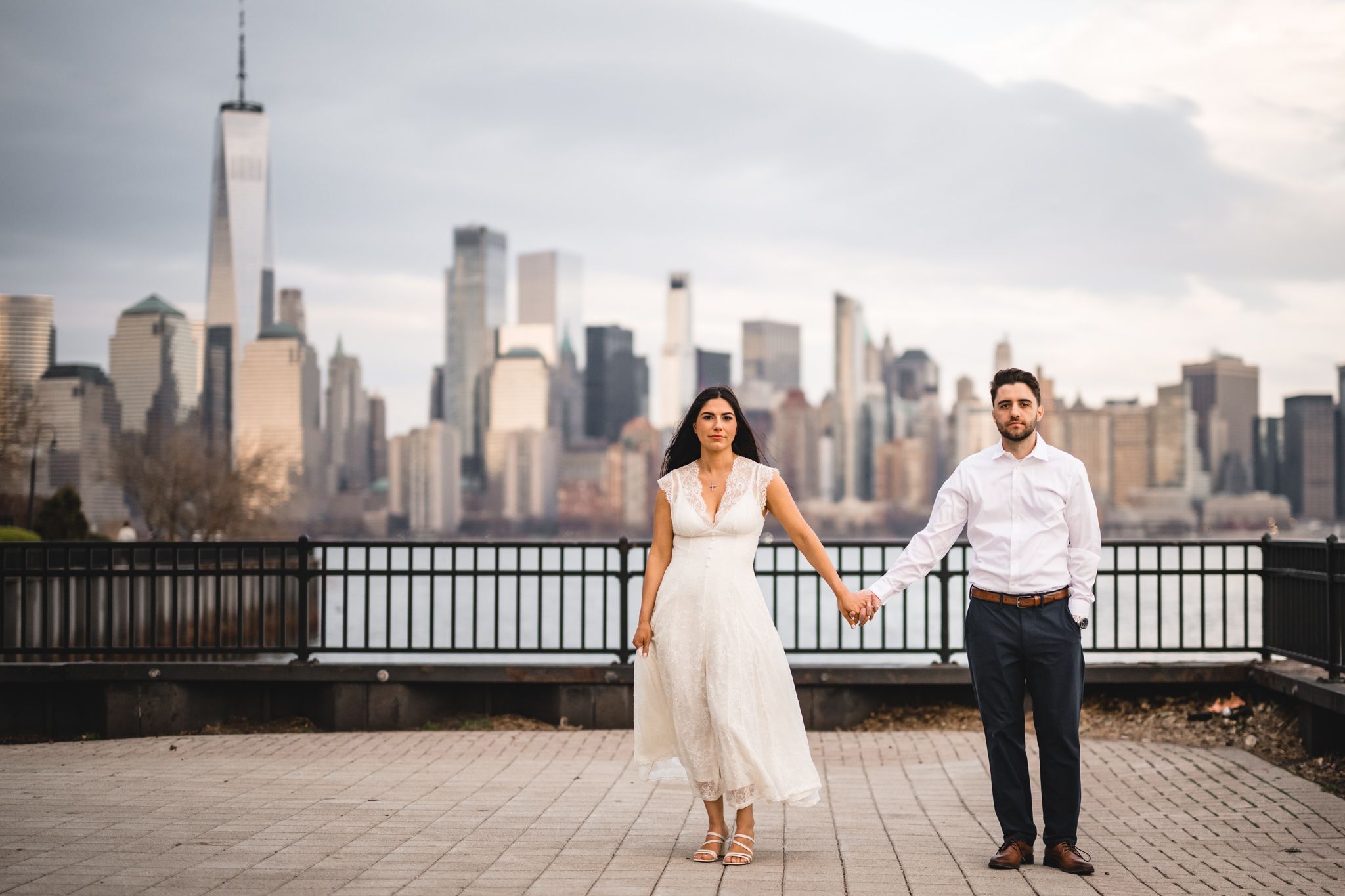 Couple holding hands with NYC skyline and One World Trade Center backdrop during engagement photo session.