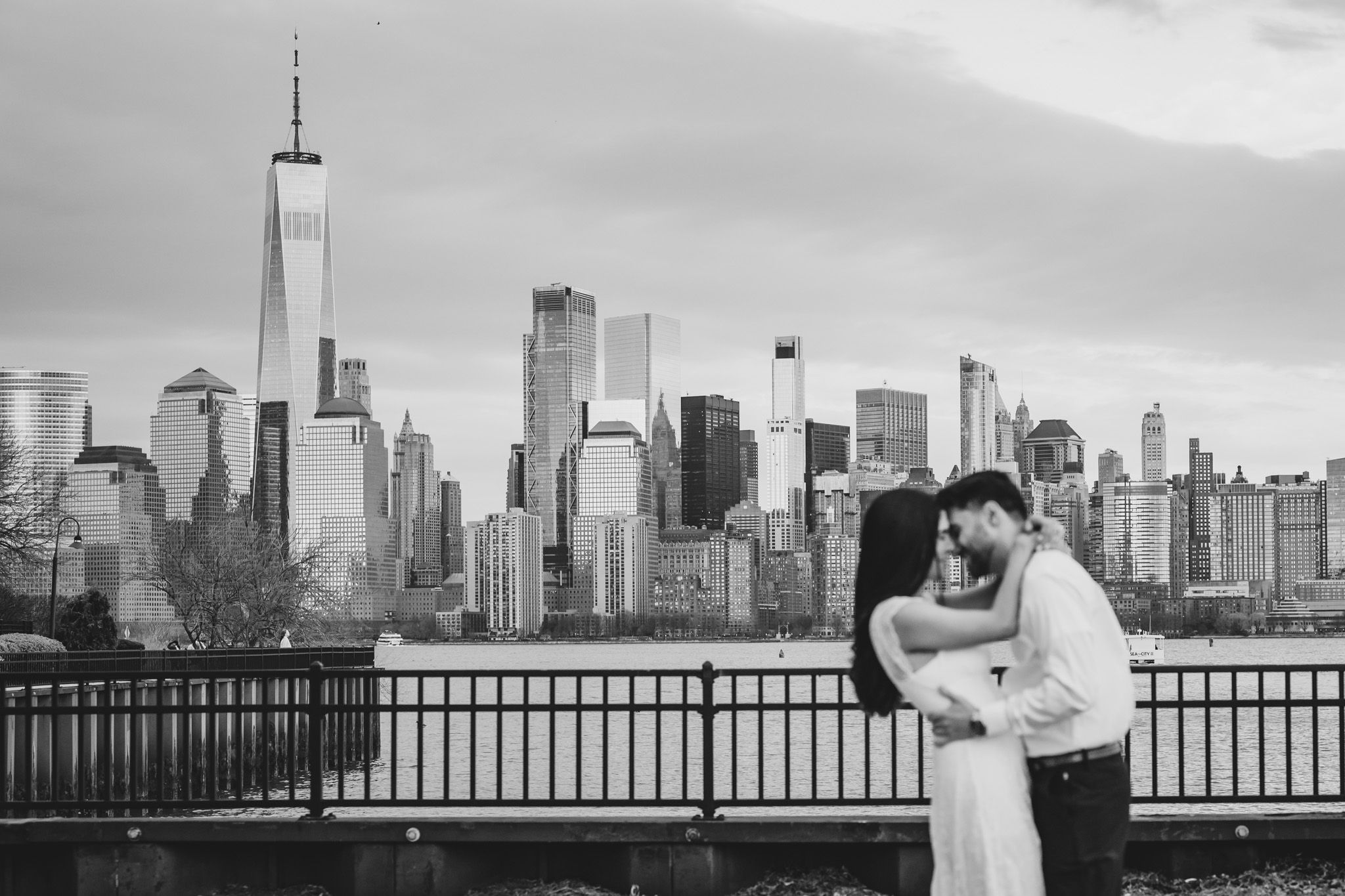 Couple embracing with NYC skyline and One World Trade Center in black and white engagement photo.